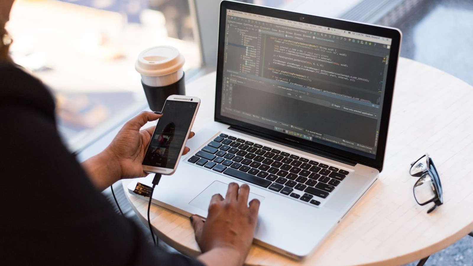 رجل يمسك هاتفًا موصولًا بكابل USB إلى كمبيوتر محمول